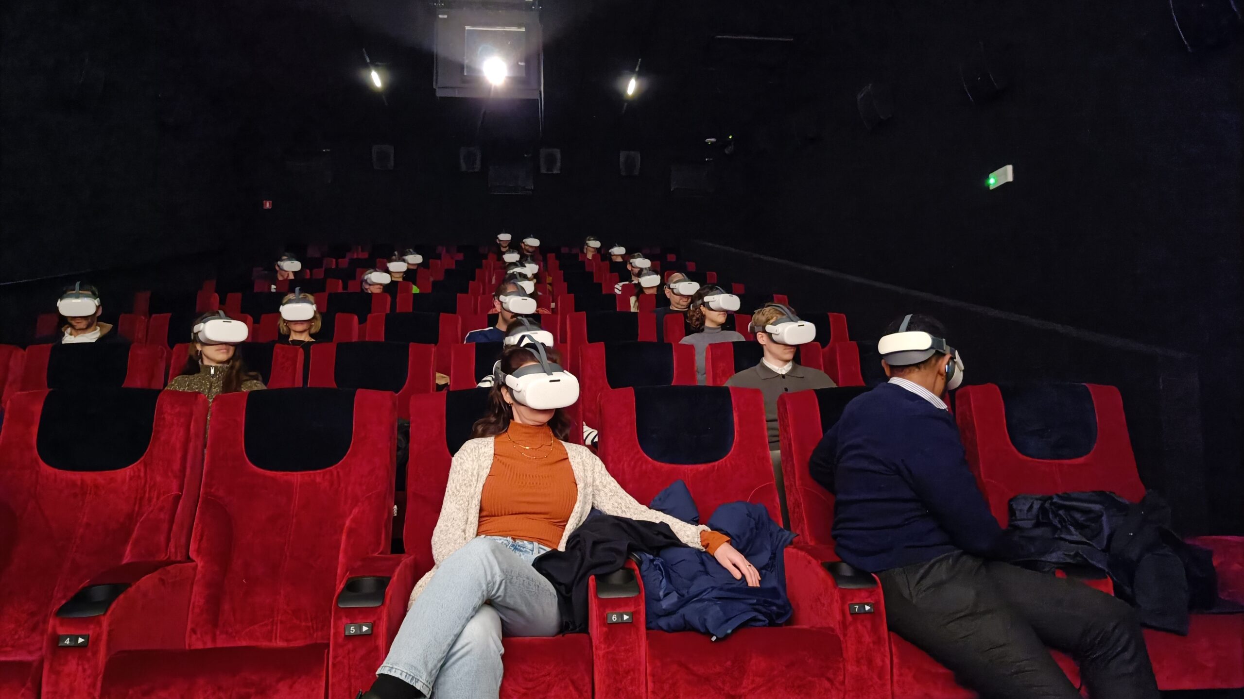 Rows of visitors in VR headsets watching a synchronised screening in a darkened cinema