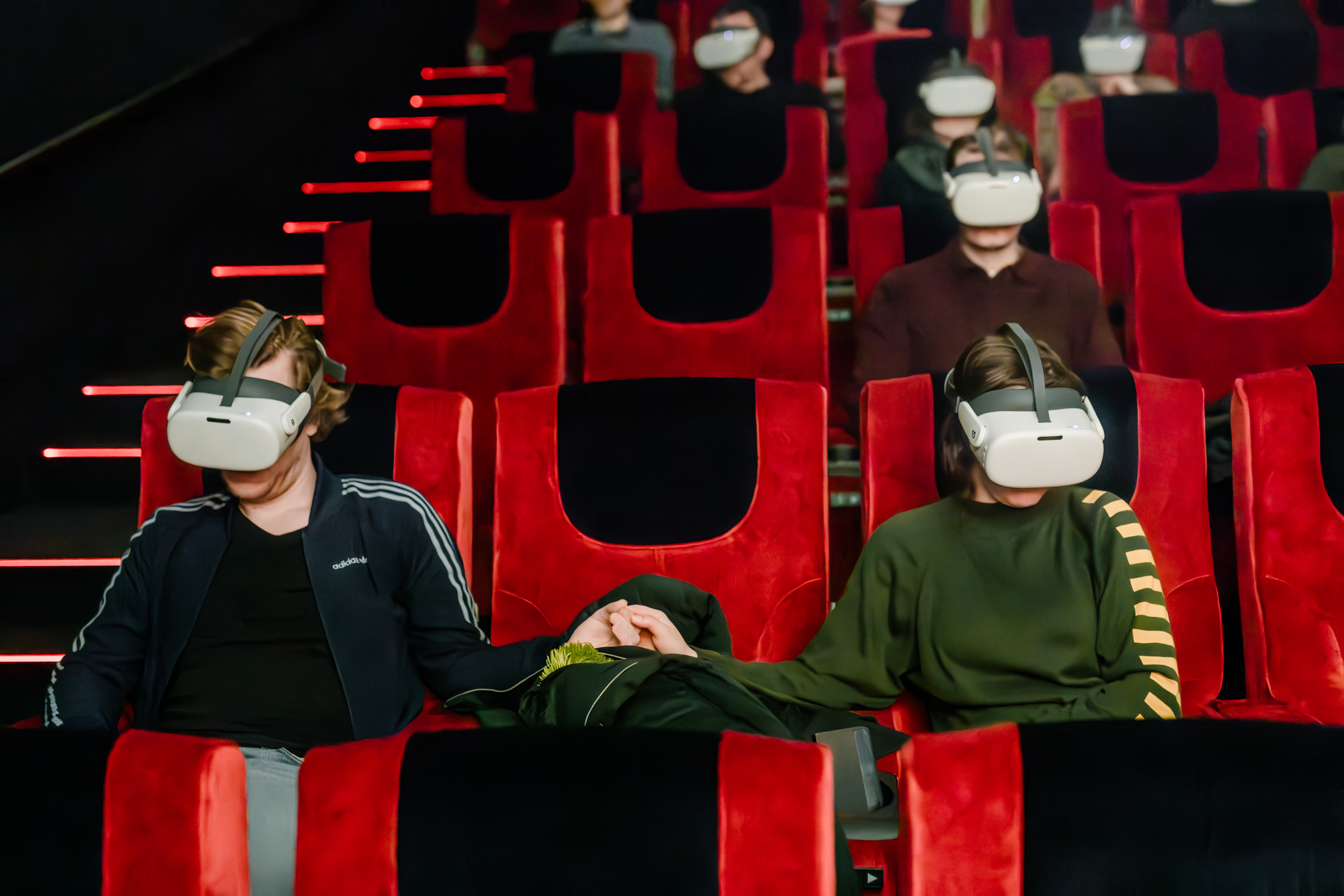 Two visitors seated in red cinema chairs wearing VR headsets during a screening.